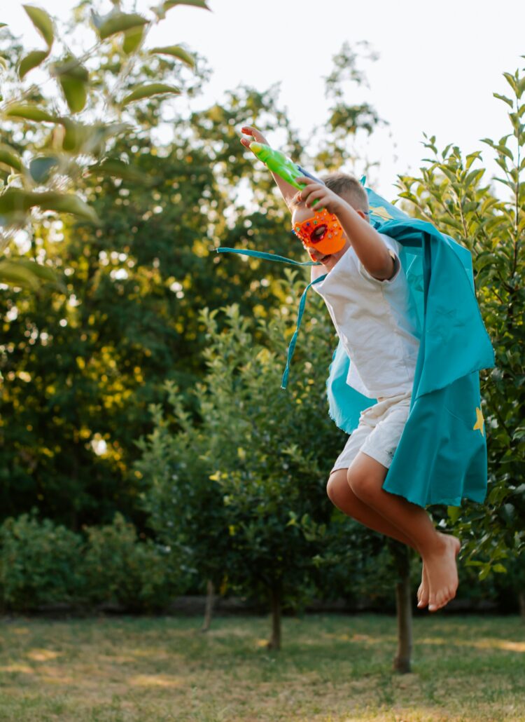 boy in super hero costume leaping over grass