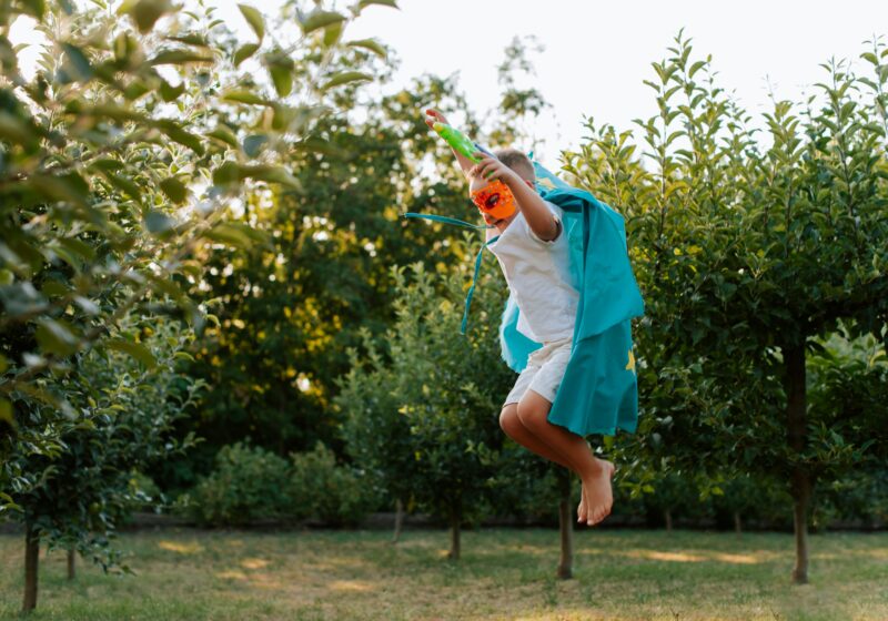 boy in super hero costume leaping over grass